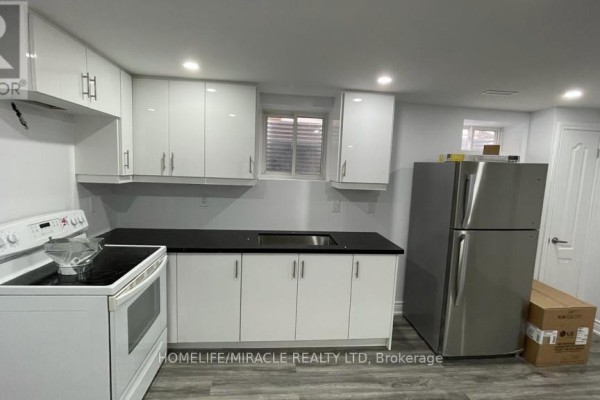 Basement kitchen with white cabinets, black countertops, stainless steel fridge, and white stove. - Bsmt - 7010 Cordingley Crescent, Mississauga
