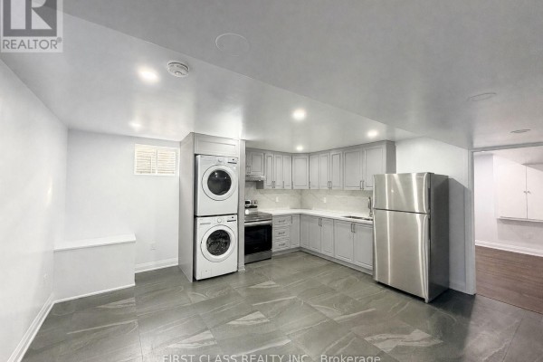 Basement kitchen with light grey cabinets, stainless steel refrigerator, stacked washer and dryer, and grey tiled floor. - Bsmt - 720 Savoline Boulevard, Milton