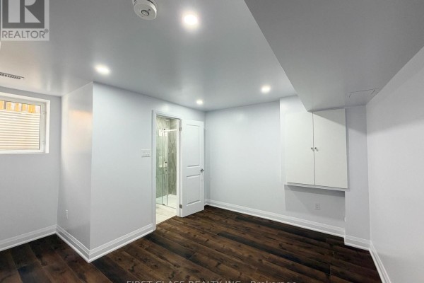 Basement bedroom with dark wood flooring, white walls, white cabinets, and a glass-enclosed shower visible through a doorway. - Bsmt - 720 Savoline Boulevard, Milton