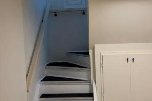 View of a narrow staircase leading down with white risers, black treads, and a wooden handrail. - Bsmt - 78 Cree Avenue, Toronto