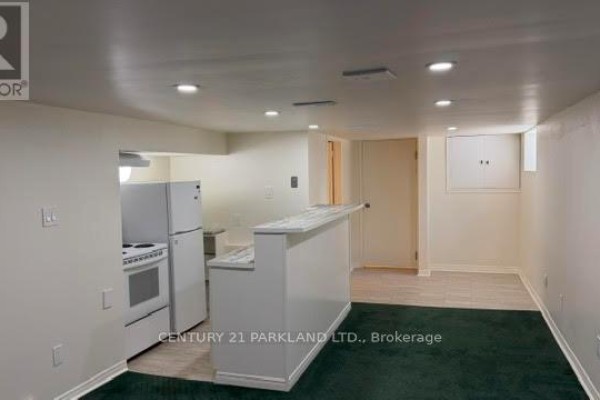 Basement living area with a small kitchen, white cabinets, refrigerator, stove, and a breakfast bar. - Bsmt - 78 Cree Avenue, Toronto