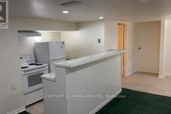 Interior view of the basement kitchen area with white appliances, counter, and adjoining living space. - Bsmt - 78 Cree Avenue, Toronto