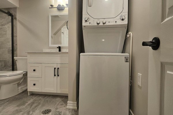 Basement bathroom with white vanity, toilet, stacked washer and dryer, and grey marble-look tile flooring. - Bsmt - 79 Mantz Crescent, Whitby