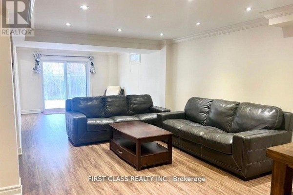 Living room with two black leather sofas, a wooden coffee table, and a sliding glass door. - Bsmt - 9 Wiley Avenue, Richmond Hill