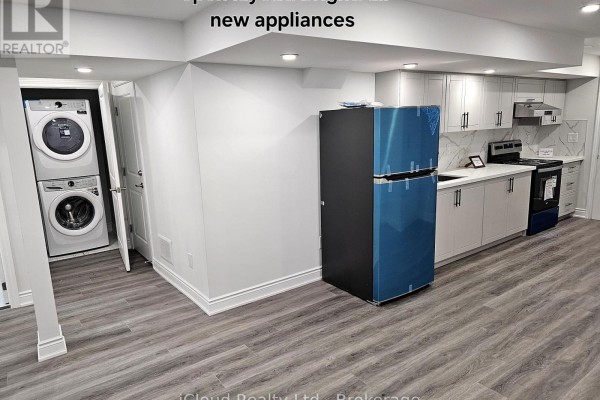 Basement living area with a stacked washer and dryer, new blue-wrapped refrigerator, and white kitchen cabinets. - Bsmt - 95 Northglen Boulevard, Clarington