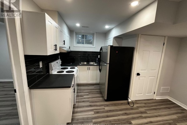 Basement kitchen with white cabinetry, black countertops, white appliances, and a black tile backsplash. - Bsmt - 96 Honey Street, Cambridge