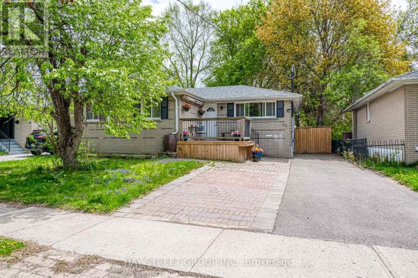 Front exterior of a light beige brick bungalow with a wooden deck and a red brick driveway. - Bsmt - 99 Cherrywood Drive, Newmarket