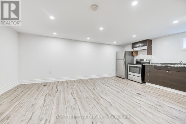 Basement living area with light wood laminate flooring and a stainless steel refrigerator and stove. - Bsmt - 99 Cherrywood Drive, Newmarket