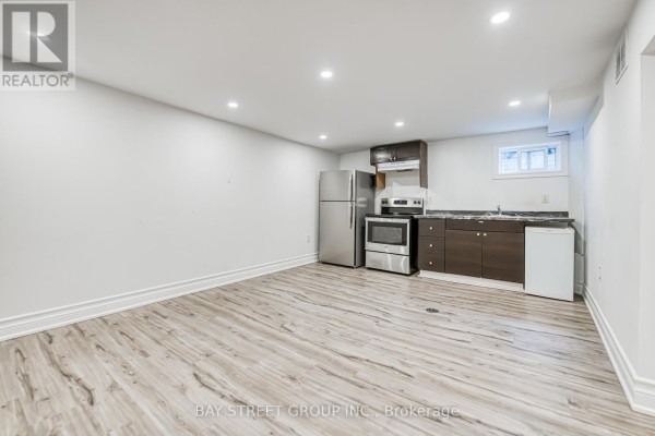 Basement living area with light wood laminate flooring, dark wood cabinets, and a small white refrigerator. - Bsmt - 99 Cherrywood Drive, Newmarket