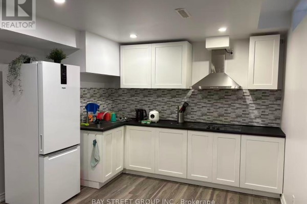 L-shaped kitchen with white cabinets, black countertops, a white refrigerator, and a tiled backsplash. - Bsmt-2 - 1966 Kempton Park Drive, Mississauga