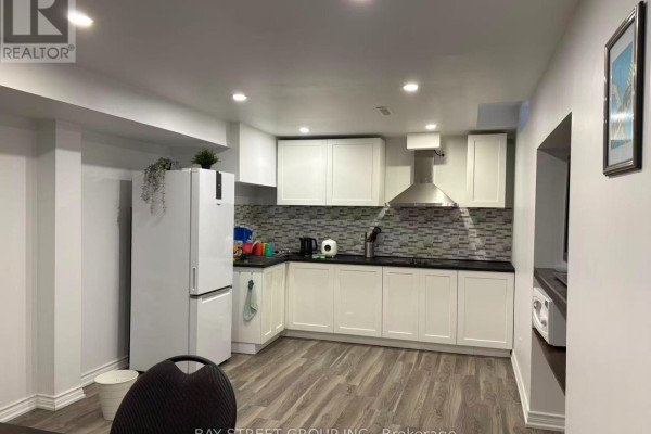 Wide view of a galley kitchen with white cabinets, black countertops, and a stainless steel range hood. - Bsmt-2 - 1966 Kempton Park Drive, Mississauga