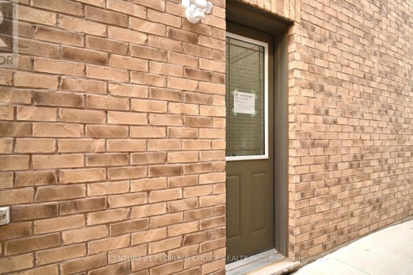 Close-up of a brown brick exterior wall with a dark green door and a window. - Bsmt 2 - 26 Lyle Way, Brampton