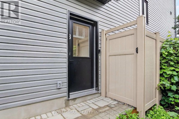 Close-up of a side exterior door with a glass pane, a beige fence, and grey siding. - Bsmt #b - 522 Mutual Street, Ottawa