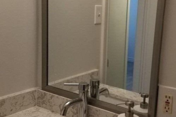 A bathroom vanity with a white countertop, chrome faucet, and a large mirror reflecting a doorway. - Bsmt Rm - 12 Flerimac Road, Toronto