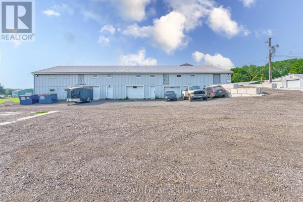 Rear exterior of a commercial building with several garage doors and vehicles. - Building #4 Upper #1 - 428 Lynden Road, Brantford