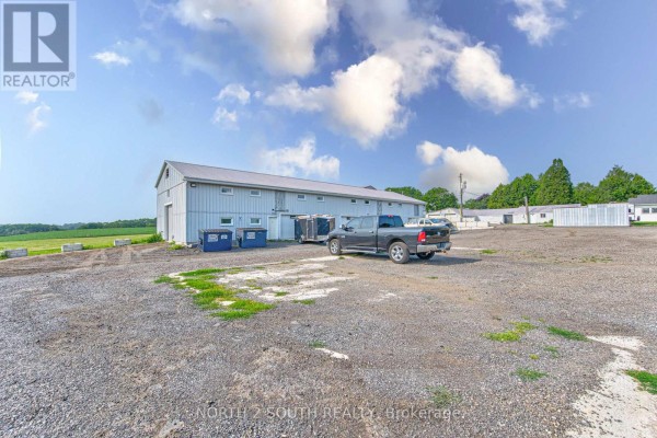 Commercial building with a gravel lot, green fields, and vehicles. - Building 4 Upper #1 & #2 - 428 Lynden Road, Brantford