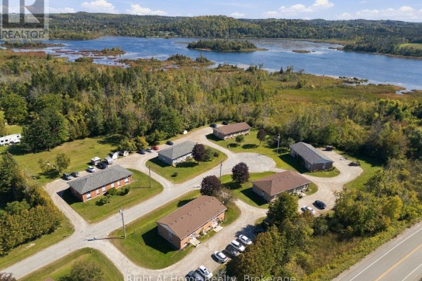 Aerial view of multiple apartment buildings set amongst trees, with a large lake visible beyond. - C - 103 Rita Crescent, Kawartha Lakes