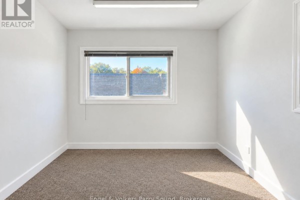 Interior office space with light blue walls, beige tiled floor, desk, chair, and shelving unit. - C - 93 James Street, Parry Sound