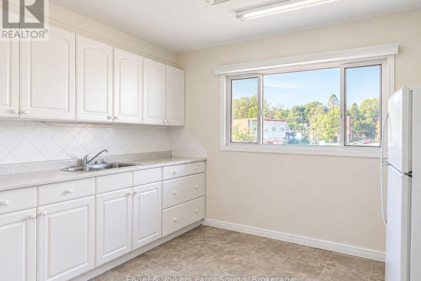 Kitchenette area with stainless steel appliances, yellow walls, and a long counter with black crates. - C - 93 James Street, Parry Sound