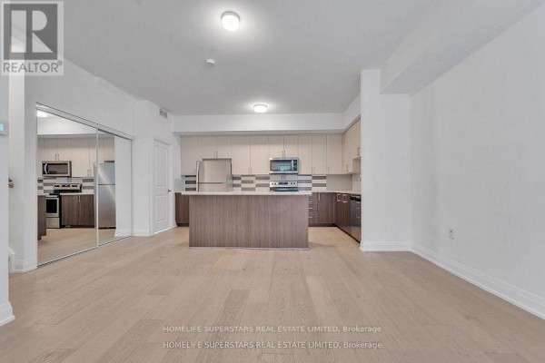 Open concept living area with a kitchen island, stainless steel appliances, and mirrored closet doors. - C-302 - 5299 Highway 7 Street, Vaughan