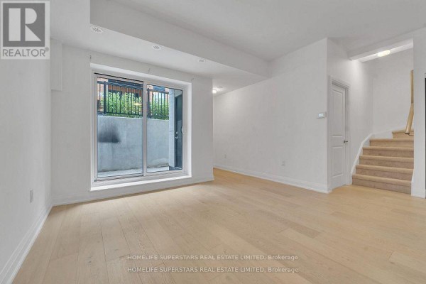 Living area with light wood floors, a glass sliding door, and stairs leading upwards. - C-302 - 5299 Highway 7 Street, Vaughan