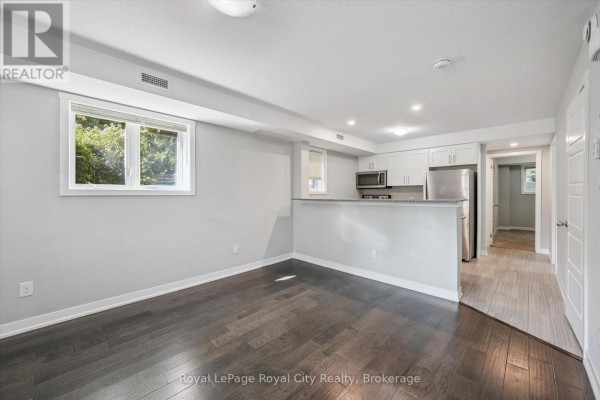 Living room and kitchen area with dark wood floors, white cabinets, stainless steel appliances, and a breakfast bar. - C1 - 190 Century Hill Drive, Kitchener