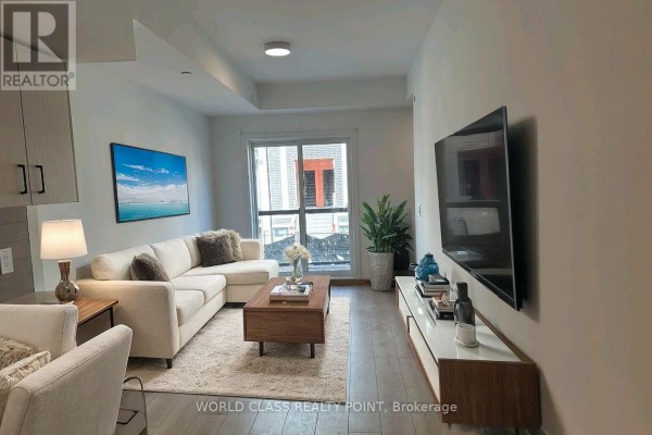 Living room with beige sectional sofa, coffee table, and mounted TV. - C3-201 - 3425 Sheppard Avenue E, Toronto