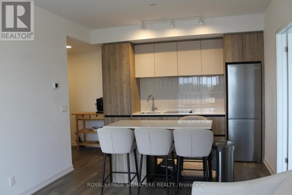 Apartment kitchen with island, stainless steel appliances, and light wood cabinets. - C701 - 8 Beverley Glen Boulevard, Vaughan