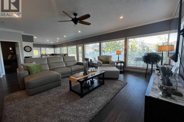 Bedroom with a queen-size bed, nightstand, and a fan near the window. - Cabin 1 155 Birch Bay Resort Road, Fraser Lake