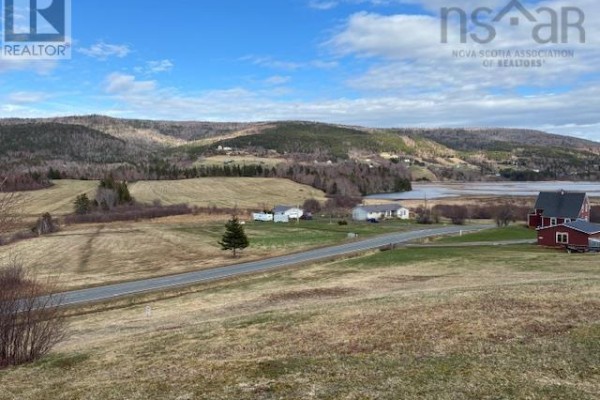 Expansive view of a rural landscape featuring a road, houses, fields, and water body with forested hills beyond. - Cabot Trail, Scotch Hill, Margaree Harbour