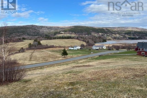 A wide view of a rural property with rolling hills, fields, water, and scattered buildings under a partly cloudy sky. - Cabot Trail, Scotch Hill, Margaree Harbour