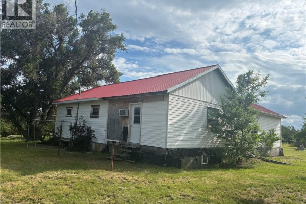 Rear view of the white house with a red metal roof, siding, and a back door. - Cantuar Acreage, Swift Current Rm No  137