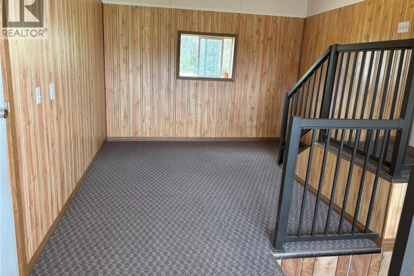 Interior room with wood-paneled walls, brown patterned carpet, and a black metal railing staircase. - Cantuar Acreage, Swift Current Rm No  137