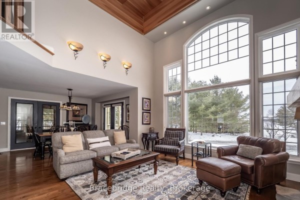 Spacious living room with high ceilings, large windows, fireplace, and furniture arranged around a rug. - Carling 10 W3 - 3876 Muskoka Rd 118 Highway W, Muskoka Lakes