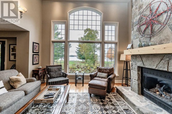 Living room with a stone fireplace, large arched window, and two sofas facing the water view. - Carling 6 W2 - 3876 Muskoka Rd 118 Highway W, Muskoka Lakes