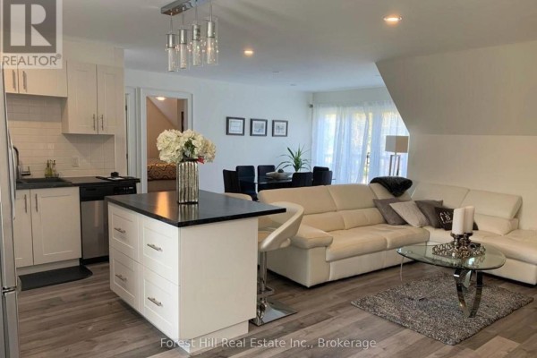 Open concept living and dining area with white sectional sofa, black dining set, and modern kitchen island. - Carriage House - 51 Louisa Street W, Blue Mountains