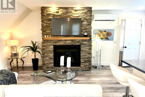 Living room fireplace with stacked stone surround, television, wood mantle, and adjacent air conditioning unit. - Carriage House - 51 Louisa Street W, Blue Mountains