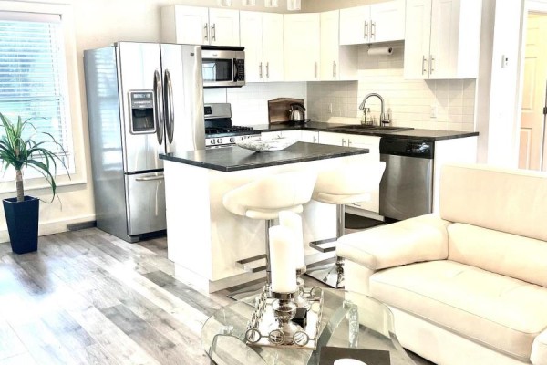 Kitchen with white cabinets, stainless steel appliances, black countertops, and breakfast bar with stools. - Carriage House - 51 Louisa Street W, Blue Mountains