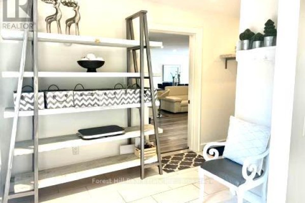 Entryway with tall ladder bookshelf, grey and white patterned storage bins, and chair with patterned rug. - Carriage House - 51 Louisa Street W, Blue Mountains