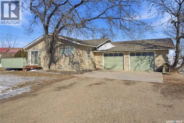 Exterior of house with tan siding, green garage doors, and mature trees. - Chamberlain Acreage 3, Chamberlain