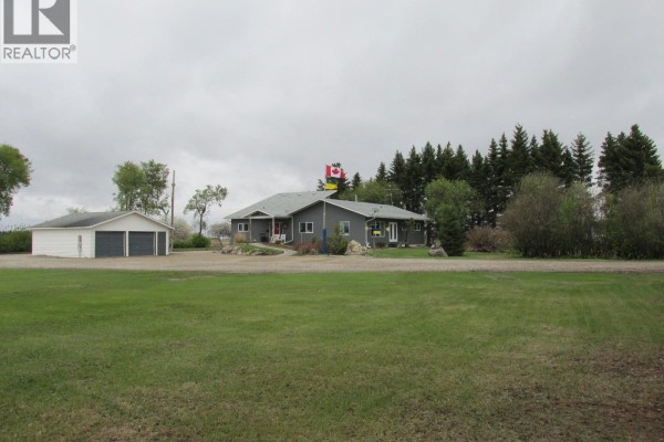 Front view of the single-story grey house with a detached two-car garage and surrounding grass. - Codette Acreage, Nipawin Rm No  487