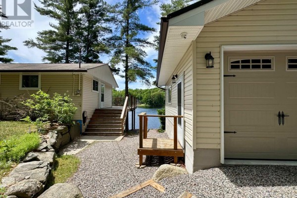 Exterior view showing the cottage, garage, and a wooden deck overlooking the water. - Cottage # 9 - 1006 Youngs Road, Muskoka Lakes