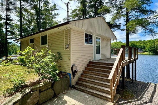 Side view of the beige cottage with a wooden deck leading to the lake. - Cottage # 9 - 1006 Youngs Road, Muskoka Lakes