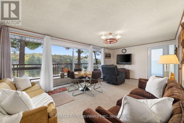 Living room with a sofa, recliner, dining table, television, and large windows overlooking the lake. - Cottage # 9 - 1006 Youngs Road, Muskoka Lakes