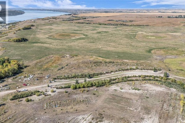 Aerial view of a treed slope leading down to cultivated fields and a distant lake. - Craven Valley Acres, Longlaketon Rm No  219