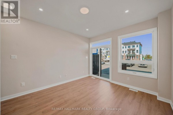 Empty room with light wood floors, beige walls, and large windows overlooking townhouses. - D - 142 Conservancy Drive, Ottawa