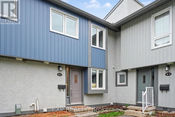 Side exterior view of the townhouse entrance with blue siding and grey stucco. - D - 32 Benlea Drive, Ottawa