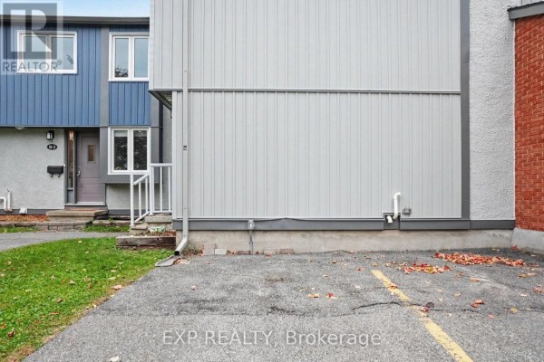 Exterior side view of townhouse with parking area and grassy lawn. - D - 32 Benlea Drive, Ottawa