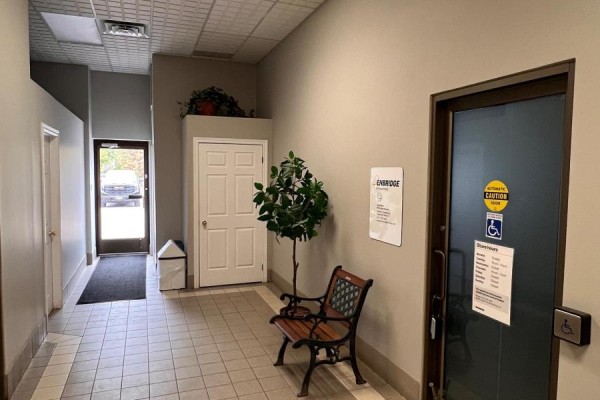 View down an interior hallway showing a door, bench, plant, and an exit sign. - D - 71 Bolton Street, Kawartha Lakes