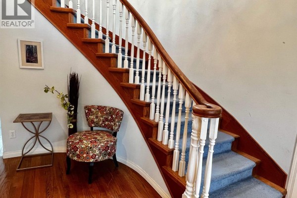 Curved staircase with white spindles, wood banister, and blue carpet runner. - D 4864 Watling Street, Burnaby